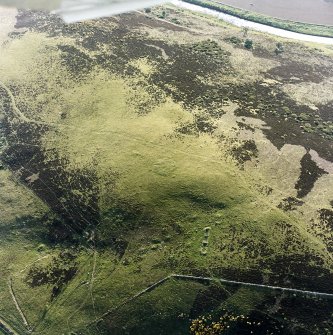 Oblique aerial view centred on the remains of the cairn and small cairns with buildings adjacent, taken from the SE.