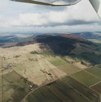 Oblique aerial view looking across the farmsteads towards the vitrified fort, taken from the SW.