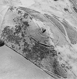 Oblique aerial view of Dunnideer centred on the remains of a fort and tower-house with rig visible on the NE slope, taken from the NW.