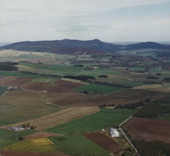 General oblique aerial view looking across the farmsteadings and cottages towards Bennachie and the remains of the fort, taken from the WSW.