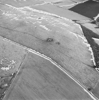 Oblique aerial view centred on the remains of the ring-cairn with rig adjacent, taken from the NW.