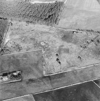 Oblique aerial view centred on the remains of the hut-circle, buildings and small cairns, taken from the SW.