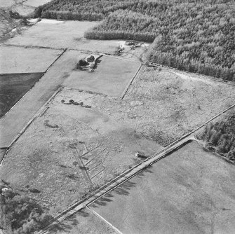 Oblique aerial view centred on the remains of the hut-circle, buildings and small cairns, taken from the E.