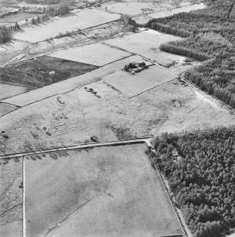 Oblique aerial view centred on the remains of the hut-circle, buildings and small cairns, taken from the NE.