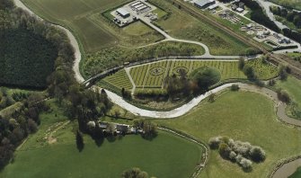 Oblique aerial view centred on the remains of the motte-and-bailey castle, burial-ground and the cemetery with the cottage adjacent, taken from the NE.