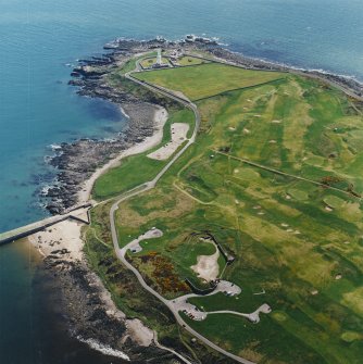 Oblique aerial view centred on the remains of the coastal battery with breakwaters adjacent and lighthouse in the distance, taken from the WNW .