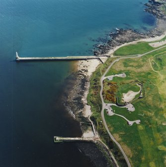 Oblique aerial view centred on the remains of the coastal battery with breakwaters adjacent, taken from the W.
