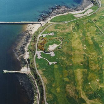 Oblique aerial view centred on the remains of the coastal battery with breakwaters adjacent, taken from the W.