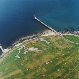 Oblique aerial view centred on the remains of the coastal battery with breakwaters adjacent, taken from the S.