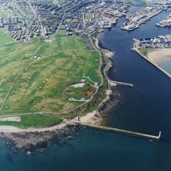 Oblique aerial view centred on the remains of the coastal battery with breakwaters adjacent, taken from the ENE.