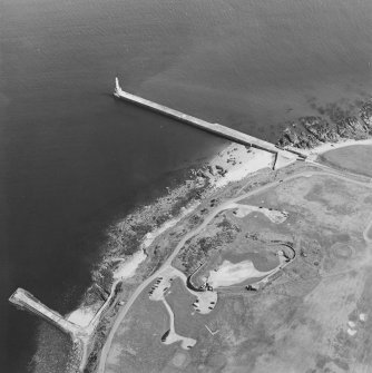 Oblique aerial view centred on the remains of the coastal battery with breakwaters adjacent, taken from the W.