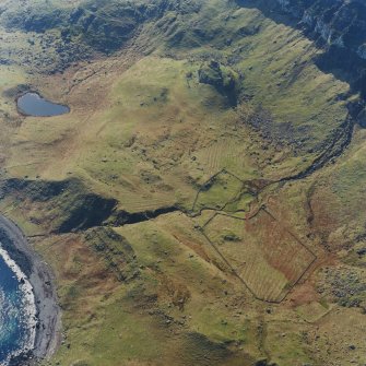 Oblique aerial view centred on the remains of the farmstead, shieling-huts and rig with fort adjacent, taken from the NE.