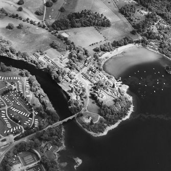 Oblique aerial view of Kenmore centred on the road bridge, church and hotel, and the remains of a crannog with Kenmore Village adjacent, taken from the W.