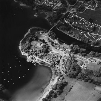 Oblique aerial view of Kenmore centred on the road bridge, church and hotel, and the remains of a crannog with Kenmore Village adjacent, taken from the ESE.