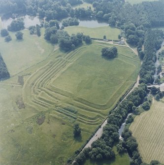 Oblique aerial view centred on the remains of the Roman Fort, chapel and burial ground, with road bridge adjacent, taken from the NNW.
