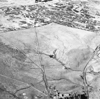 Corrymuckloch, oblique aerial view, taken from the SSW, showing the Crieff to Dalnacardoch military road running across the centre of the photograph. An area of hut-circles, clearance cairns and field banks is visible in the centre. A hoard find spot, in peat cuttings, is visible as a dark patch in the centre of the photograph.