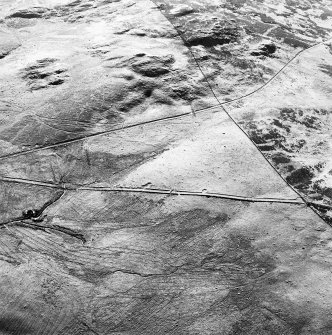 Corrymuckloch, oblique aerial view, taken from the ESE, showing the Crieff to Dalnacardoch military road running across the centre of the photograph. An area of hut-circles, clearance cairns and field banks is visible in the centre. A hoard find spot, in peat cuttings, is visible as a dark patch in the centre left of the photograph.