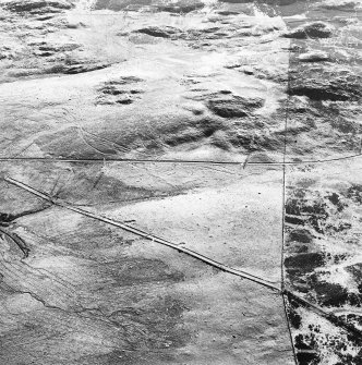 Corrymuckloch, oblique aerial view, taken from the ESE, showing the Crieff to Dalnacardoch military road running across the centre of the photograph. An area of hut-circles, clearance cairns and field banks is visible in the centre. A hoard find spot, in peat cuttings, is visible as a dark patch in the centre left of the photograph.