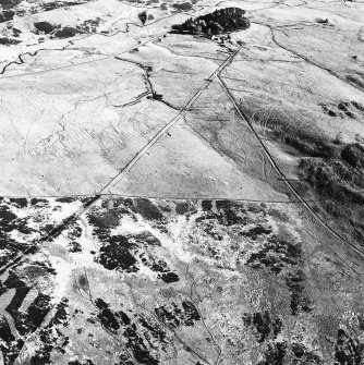 Corrymuckloch, oblique aerial view, taken from the NNW, showing the Crieff to Dalnacardoch military road running across the centre of the photograph. An area of hut-circles, clearance cairns and field banks is visible in the centre. A hoard find spot, in peat cuttings, is visible as a dark patch in the top centre of the photograph.