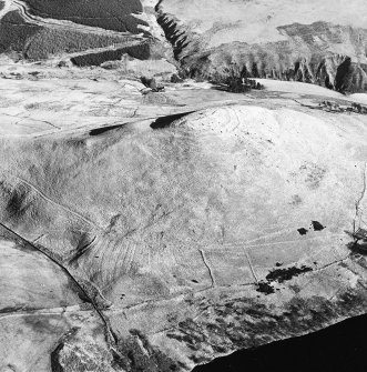 Oblique aerial view centred on the remains of a field-system and rig on the slopes below the fort, taken from the W.