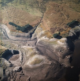 Oblique aerial view centred on the remains of farmsteads, enclosures and sheepfold with quarry and sheep shelter adjacent, taken during low water from the NE.