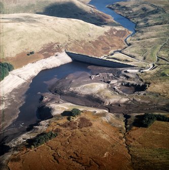 Oblique aerial view centred on the reservoir dam with quarrying associated with its construction, farmsteads, sheepfold and enclosures adjacent, taken during low water from the WSW.