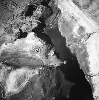 Oblique aerial view centred on the remains of the farmstead and sheepfold with another farmstead and enclosures adjacent, taken during low water from the ESE.