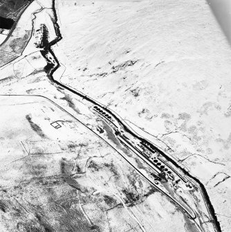 Oblique aerial view centred on the remains of buildings, enclosure, hut and lazy-beds with huts, enclosures, field-system, plantation bank, sheepfold, quarry, trackways, farmstead and field banks adjacent, taken from the W.