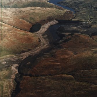 General oblique aerial view centred on the reservoir with quarry, farmsteads, enclosures, sheepfold and possible motte adjacent, taken during low water from the WNW.