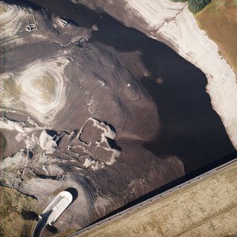 Oblique aerial view centred on the reservoir dam with quarrying associated with its construction, farmsteads, sheepfold and enclosures adjacent, taken during low water from the SE.