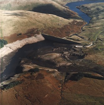 Oblique aerial view centred on the reservoir dam with quarrying associated with its construction, farmsteads, sheepfold and enclosures adjacent, taken during low water from the WSW.