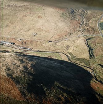 Oblique aerial view centred on the remains of the farmstead, sheepfold, rig and field-system with trackways and plantation bank adjacent, taken from the SE.