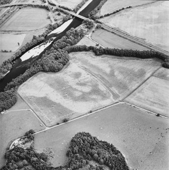Oblique aerial view centred on the site of the castle, the cropmarks of the fort, rig and the enclosures taken from the NW.