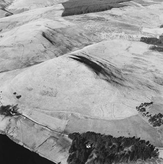 Oblique aerial view centred on the remains of the fort with a farmstead, field-systems and rig on the slopes below, taken from the S.