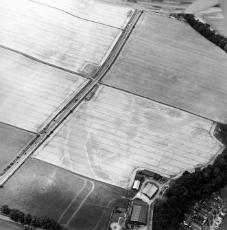 Oblique aerial view of the cropmarks of the enclosure, pits, ring-ditch, pit-alignment and Roman Road, taken from the ENE.