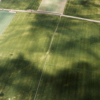 Oblique aerial view centred on the faint cropmarks of an enclosure with linear cropmarks adjacent, taken from the SSE.