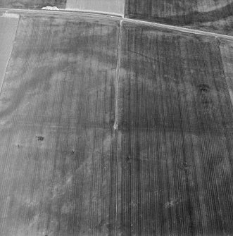 Oblique aerial view centred on the faint cropmarks of an enclosure with linear cropmarks adjacent, taken from the S.