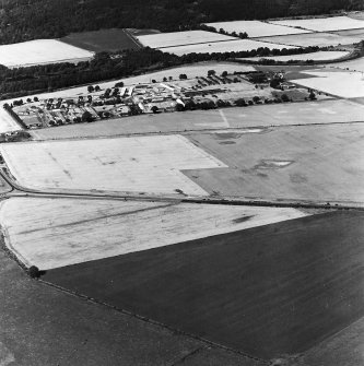 Brickhall, oblique aerial view, taken from the SSW, showing linear cropmarks running up the centre of the photograph. Bridge of Earn hospital is visible in the background.