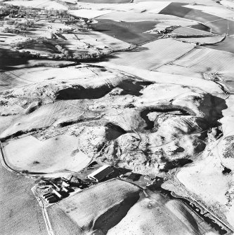 Oblique aerial view centred on the remains of enclosures, rig, fort, hut-circles, cairn, building and fermtoun, taken from the ESE.