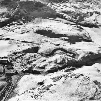 Oblique aerial view centred on the remains of enclosures, rig, fort, hut-circles, cairn, building and fermtoun, taken from the NE.