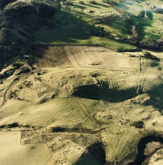 Oblique aerial view centred on the remains of the fort, hut-circles and cairn with hut-circle, enclosures, building and rig adjacent, taken from the E.