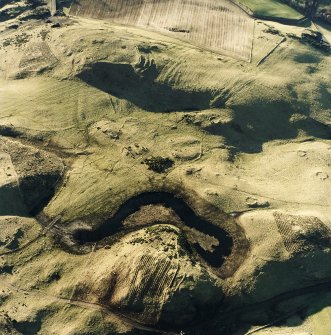 Oblique aerial view centred on the remains of rig and enclosures with fort, hut-circles, cairn, building and rig adjacent, taken from the ENE.