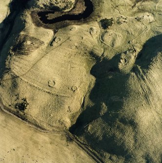 Oblique aerial view centred on the remains of hut-circles with rig and enclosures adjacent, taken from the NW.