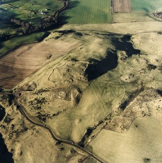 Oblique aerial view centred on the remains of the fort, hut-circles, cairn, building, enclosures and rig with enclosure and hut-circles adjacent, taken from the SE.