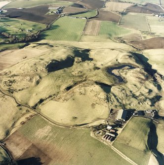 Oblique aerial view centred on the remains of rig and enclosures with fort, hut-circles, cairn, building, enclosure, rig and fermtoun adjacent, taken from the SE.