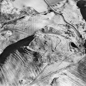 Oblique aerial view centred on the remains of the fort, hut-circles and cairn with hut-circle, enclosures, building and rig adjacent, taken from the WNW.