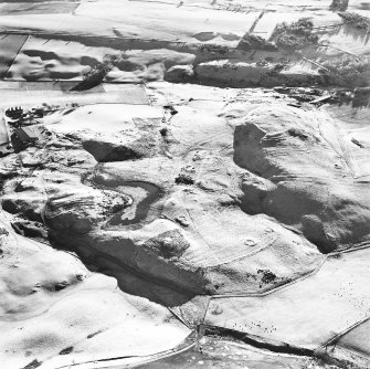 Oblique aerial view centred on the remains of enclosures, rig, fort, hut-circles, cairn, building and fermtoun, taken from the NNW.