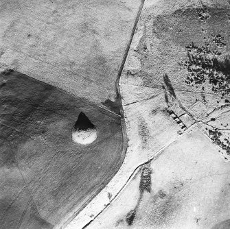 Oblique aerial view centred on the remains of the cairn with farmstead adjacent, taken from the SW.