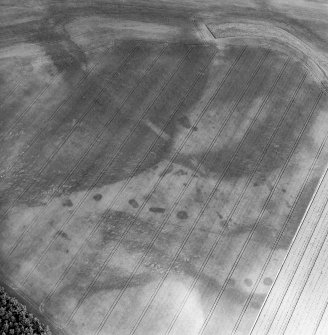 Oblique aerial view centred on the cropmarks of the quarry pits flanking a Roman Road with linear cropmarks and unenclosed settlement adjacent, taken from the SW.