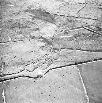 Oblique aerial view centred on the remains of the fermtoun with the remains of the buildings and hut circles, taken from the WSW.